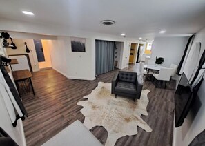 A modern living room with a leather sofa, a cowhide rug, and a dining area with white chairs. - Hamilton Hideaway | Walk to Beach & Fire Pit (Gary)