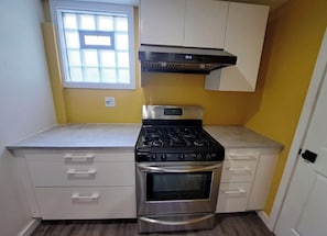 A compact kitchen with a gas stove, oven, and white cabinetry. - Hamilton Hideaway | Walk to Beach & Fire Pit (Gary)