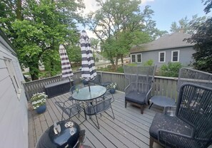 A deck with a round table, two chairs, and two striped umbrellas. - Hamilton Hideaway | Walk to Beach & Fire Pit (Gary)