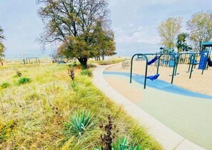A park with a walking path, playground equipment, and a tree. - Hamilton Hideaway | Walk to Beach & Fire Pit (Gary)