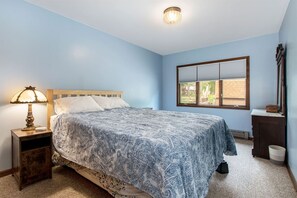 A bedroom with a bed, a nightstand, a lamp, a dresser, and a window. - Hillside Cottage | 90 Ft Lake Frontage & Beach (Lawton)
