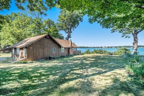 Een houten hut met een veranda, een gazon en uitzicht op het water.