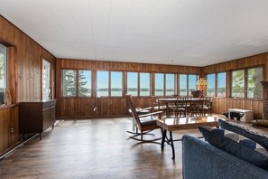 A spacious room with wooden walls and large windows offering a view of the outdoors. - Hillside Cottage | 90 Ft Lake Frontage & Beach (Lawton)