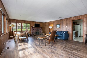 A spacious room with a wooden floor, a dining table with chairs, a sofa, and a fireplace. - Hillside Cottage | 90 Ft Lake Frontage & Beach (Lawton)