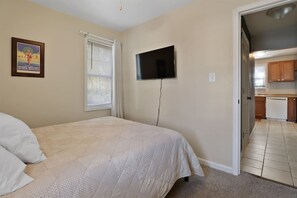 A bedroom with a bed, a television mounted on the wall, and a window with blinds. - Lafayette House | Classic Charm & Beach Minutes Away (Michigan City)