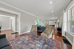 A spacious living room with hardwood floors, a large patterned rug, two armchairs, a sofa, and a blue accent wall. - The Veranda — A Timeless Michigan City Classic (Michigan City)