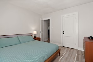 Ein Schlafzimmer mit einem Bett, einem Nachttisch, einer Lampe, einem Kleiderschrank und einer Tür zu einem weiteren Raum.