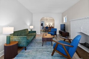 Ein modernes Wohnzimmer mit Sofa, Sessel, Couchtisch und Lampe. An der Wand befindet sich ein Kamin mit weißer Ziegeloptik.