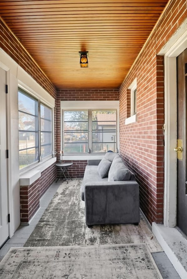 A covered porch with a brick wall, a grey sofa, and a small table.