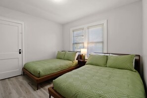 A bedroom with two single beds, a nightstand with a lamp, and a door. - Main Street Retreat | Mid-century charm steps from the lake and arts district (Michigan City)