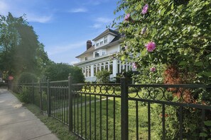 A two-story house with a white exterior, a black metal fence, and a pathway leading to the house. - The Mayor’s Mansion Private Historic Estate with (Michigan City)