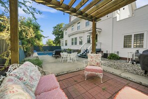 A covered patio area with outdoor furniture, a pool, and a house in the background. - The Mayor’s Mansion Private Historic Estate with (Michigan City)