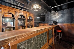 Un espace bar avec un comptoir en bois, des tabourets et un mur en briques noires.