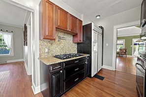 A kitchen with wooden cabinets, a granite countertop, and a stainless steel range hood. - The Mayor’s Mansion Private Historic Estate with (Michigan City)