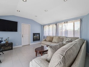 Ein Wohnzimmer mit einer Couch, einem Couchtisch, einem Kamin und einem an der Wand befestigten Fernseher.