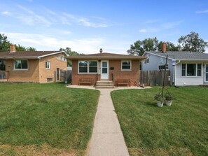 A two-story house with a front porch, a pathway leading to the door, and a small garden area with potted plants. - Mi Casa Dune Casa | Hot Tub, Pool Table & Steps to the Dunes (Gary)