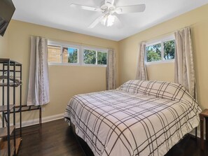 A bedroom with a bed, a ceiling fan, a window with curtains, and a wooden floor. - Mi Casa Dune Casa | Hot Tub, Pool Table & Steps to the Dunes (Gary)