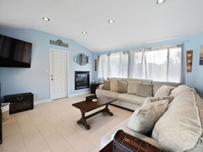 A living room with a sofa, a coffee table, a fireplace, and a television. - Mi Casa Dune Casa | Hot Tub, Pool Table & Steps to the Dunes (Gary)