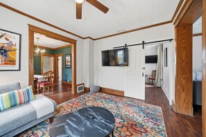 A spacious living room with a sofa, a coffee table, a patterned rug, and a television mounted on the wall. - Pine Street Flat | Steps to Everything (Michigan City)