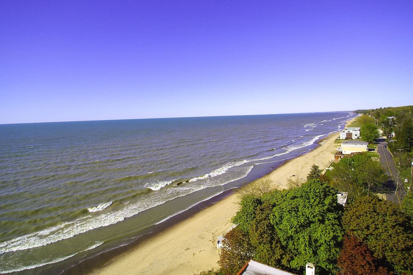 A beach with waves, a clear sky, and houses along the shore.