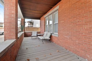 Une véranda couverte avec un mur en briques, une terrasse en bois et deux chaises.
