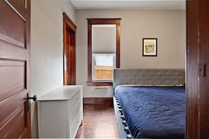 A bedroom with a bed, a radiator, a window with blinds, and a picture on the wall. - The Porch | Craftsman Charm & Steps to Downtown (Michigan City)