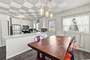 A modern kitchen with white cabinets, stainless steel appliances, and a wooden dining table with colorful chairs. - Prairie Retreat at Stop 1 (Michigan City)