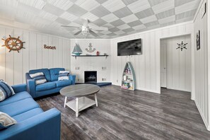 A living room with a blue sofa, a round coffee table, a fireplace, a television mounted on the wall, and nautical-themed decor. - Prairie Retreat at Stop 1 (Michigan City)