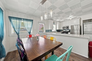 A modern kitchen with white cabinets, stainless steel appliances, and a wooden dining table with colorful chairs. - Sheridan Beach Bungalow (Michigan City)