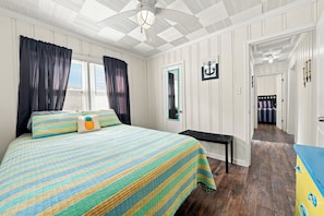 A bedroom with a bed, a bench, a door with a mirror, and a hallway leading to another room. - Sheridan Beach Bungalow (Michigan City)
