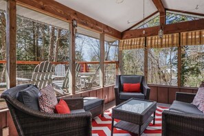 A covered outdoor seating area with wicker furniture and large windows. - The Tree House | Lake Views & Beach a Block Away (Sawyer)