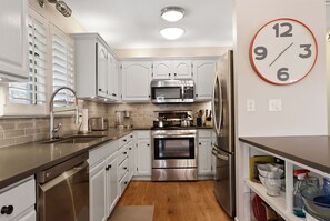 A modern kitchen with white cabinetry, stainless steel appliances, and a large wall clock. - The Tree House | Lake Views & Beach a Block Away (Sawyer)