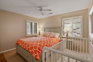 A bedroom with a bed, a nightstand, a lamp, a ceiling fan, and a crib. - The Tree House | Lake Views & Beach a Block Away (Sawyer)