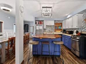 A modern kitchen with a central island, bar stools, a stove, and a refrigerator. - Wasting Time at Stop 4 | Steps to Lake Michigan (Michigan City)