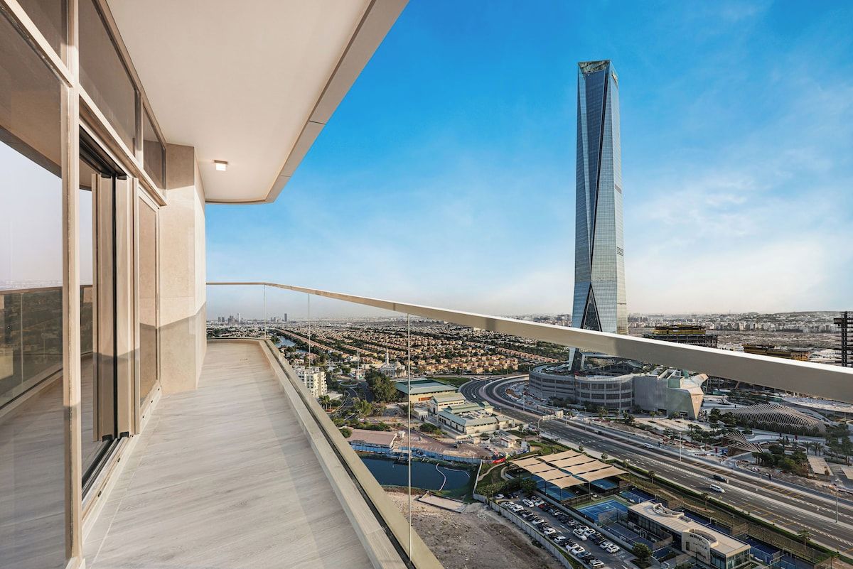 Um edifício alto com design moderno, uma varanda com guarda-corpo de vidro e vista para o horizonte urbano com uma torre imponente.