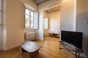 A room with a wooden floor, a bench, a flat-screen TV on a stand, and a radiator. - Colonna Suite by MMega (Firenze)