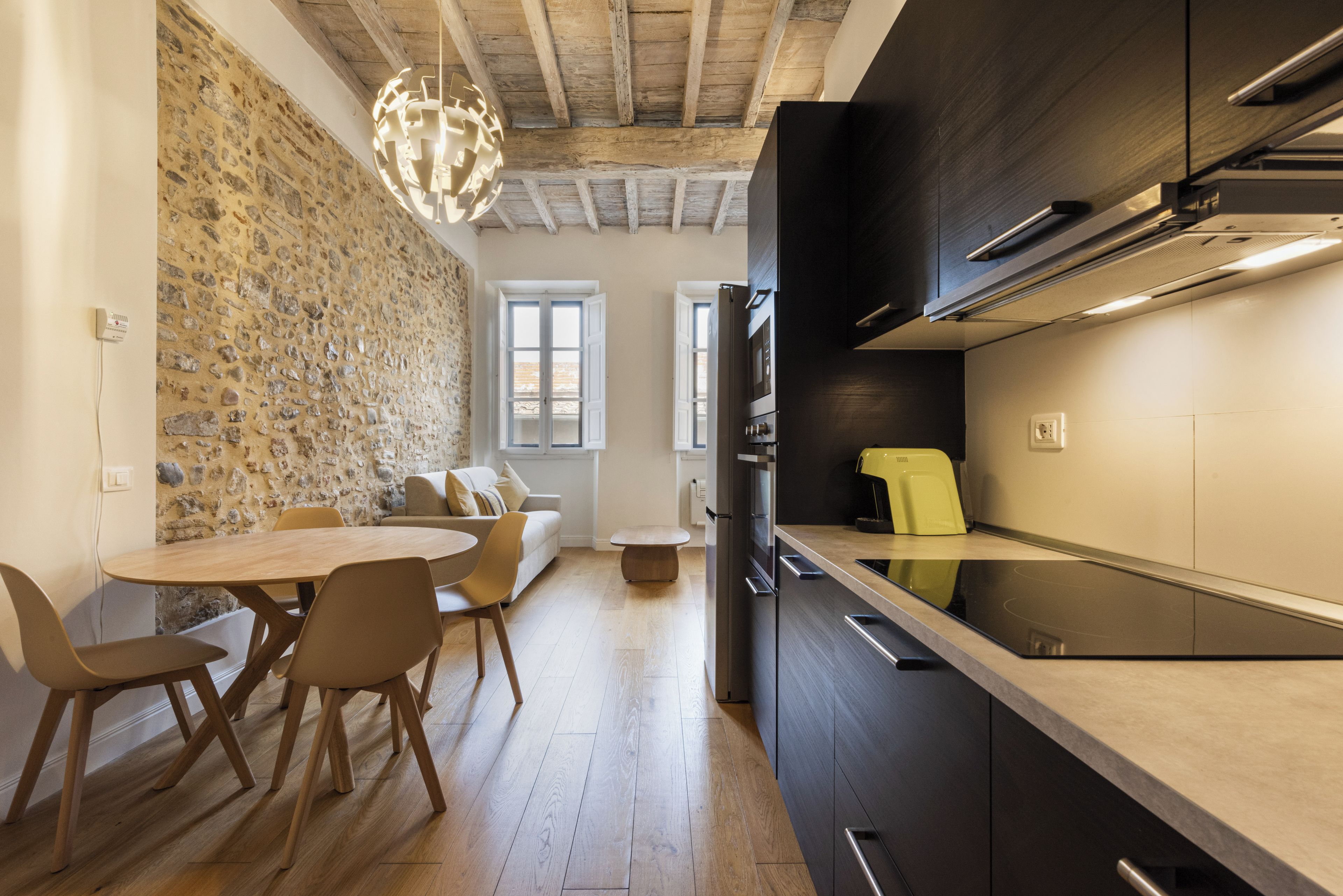 A modern kitchen with dark cabinetry, a built-in oven, and a yellow kettle.
