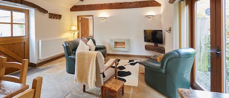 A cozy living room with a fireplace, leather sofas, a television, and a stone-tiled floor.