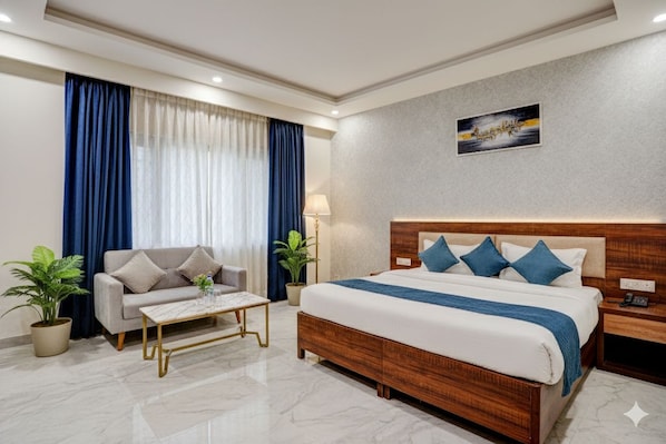 Una habitación de hotel con una cama, un sofá, una mesita de centro y una planta en maceta.