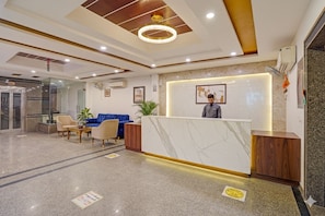 A hotel reception area with a marble reception desk, a blue sofa, and a wooden reception counter. - Hotel Clayton Suites  (DELHI)