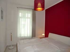 Ein Hotelzimmer mit einem Bett, einer Nachttischlampe, einer Stehlampe und einem Fenster mit Vorhängen.