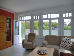 Ein Wohnzimmer mit einer Couch, Sesseln, einem Couchtisch und großen Fenstern.