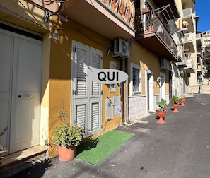A yellow building with white shutters, a green awning, and potted plants. - New Listing (Gela)