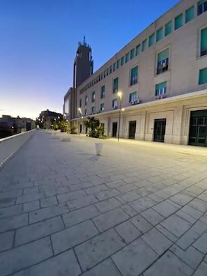 A paved outdoor area with a building featuring multiple windows and a tower. - New Listing (Gela)