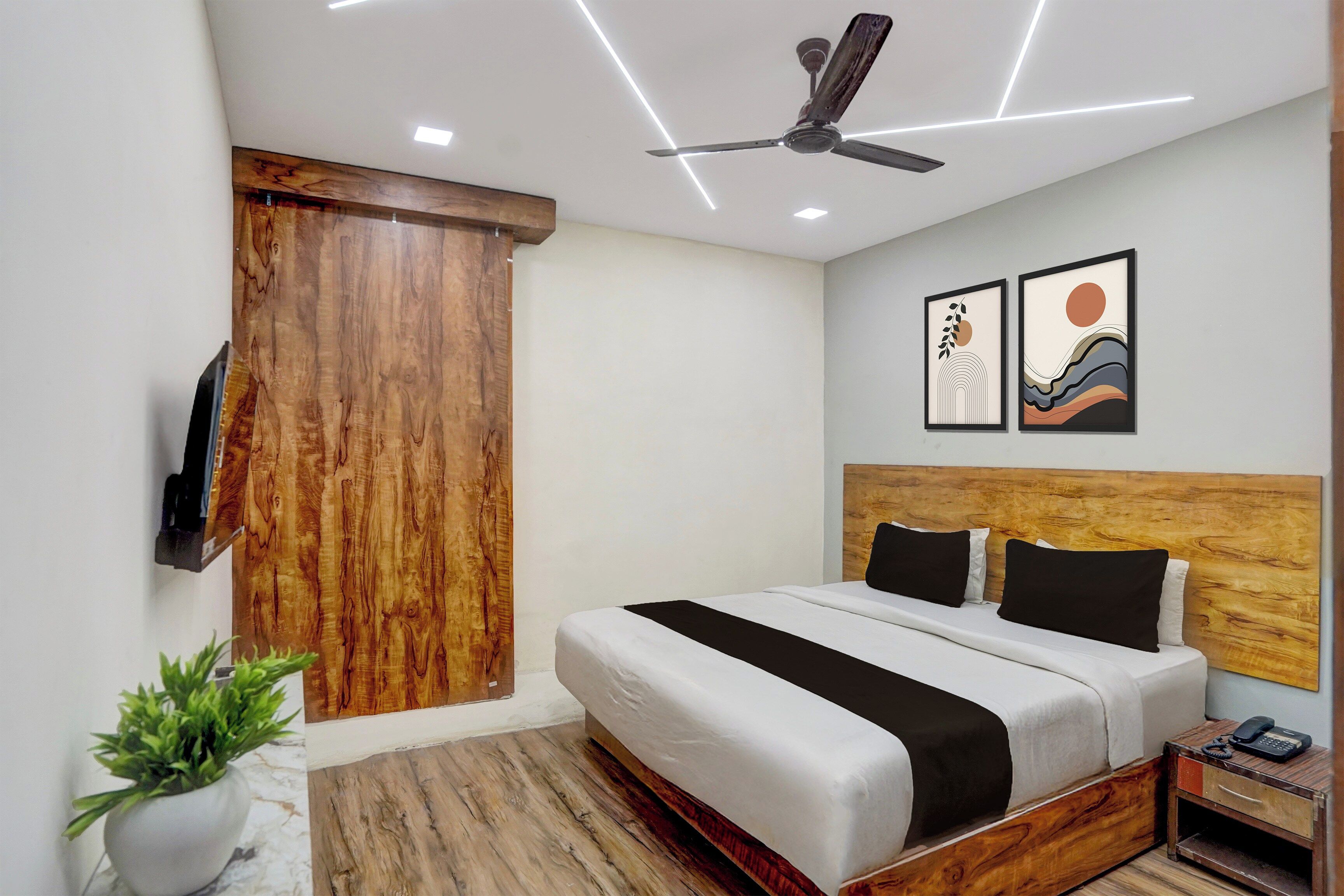 A hotel room with a bed, a ceiling fan, a wooden headboard, a nightstand, a telephone, and a wall-mounted TV.