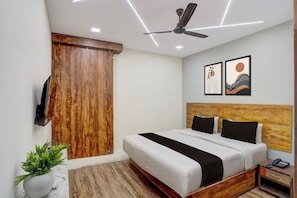 Ein Hotelzimmer mit Bett, Deckenventilator, Holz-Kopfteil, Nachttisch, Telefon und Wand-Fernseher.
