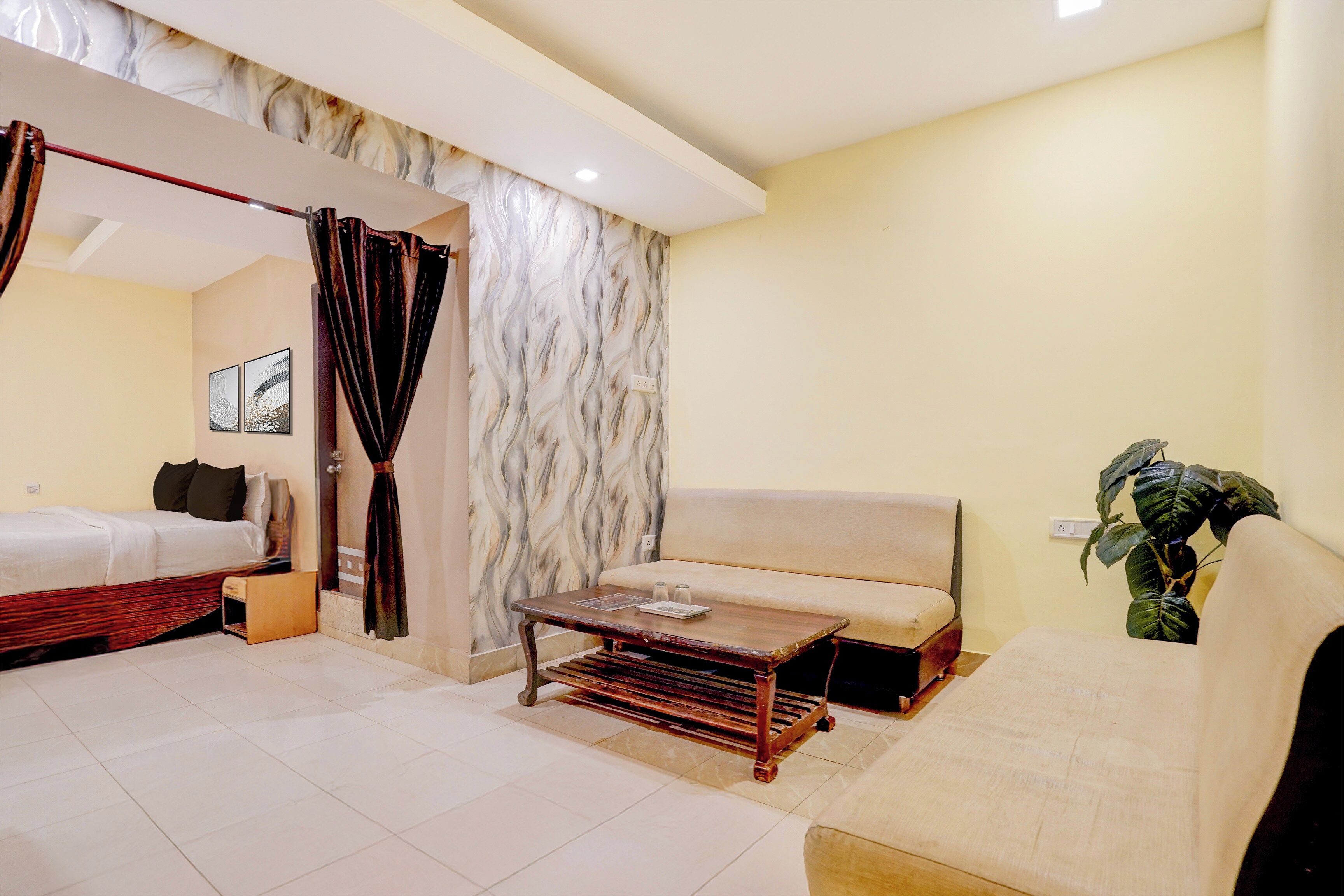 A hotel room with a bed, a sofa, a small table, and a potted plant.