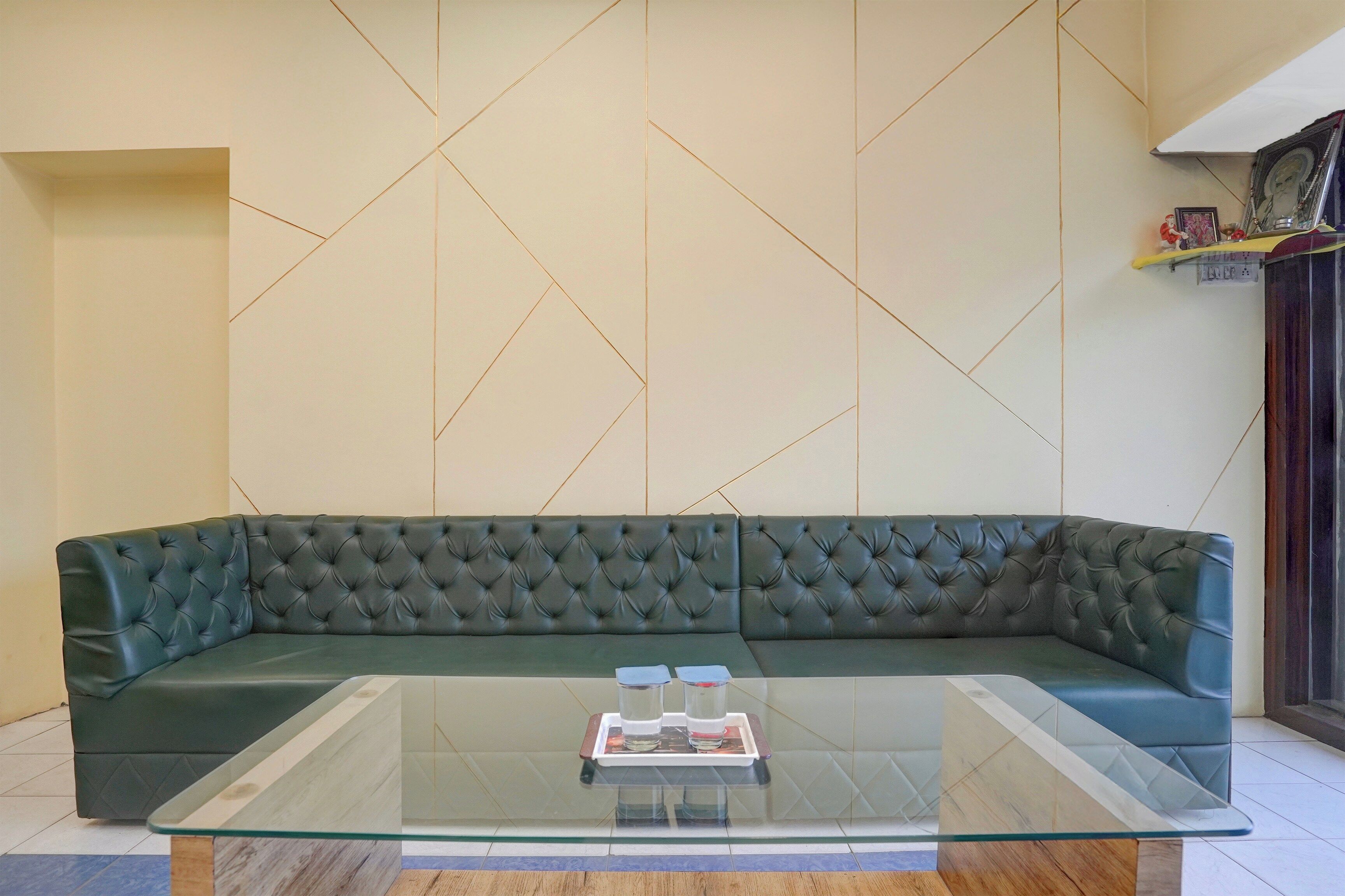 Una sala moderna con un sofá verde oscuro, una mesa de centro de cristal y una pared con estampado geométrico.