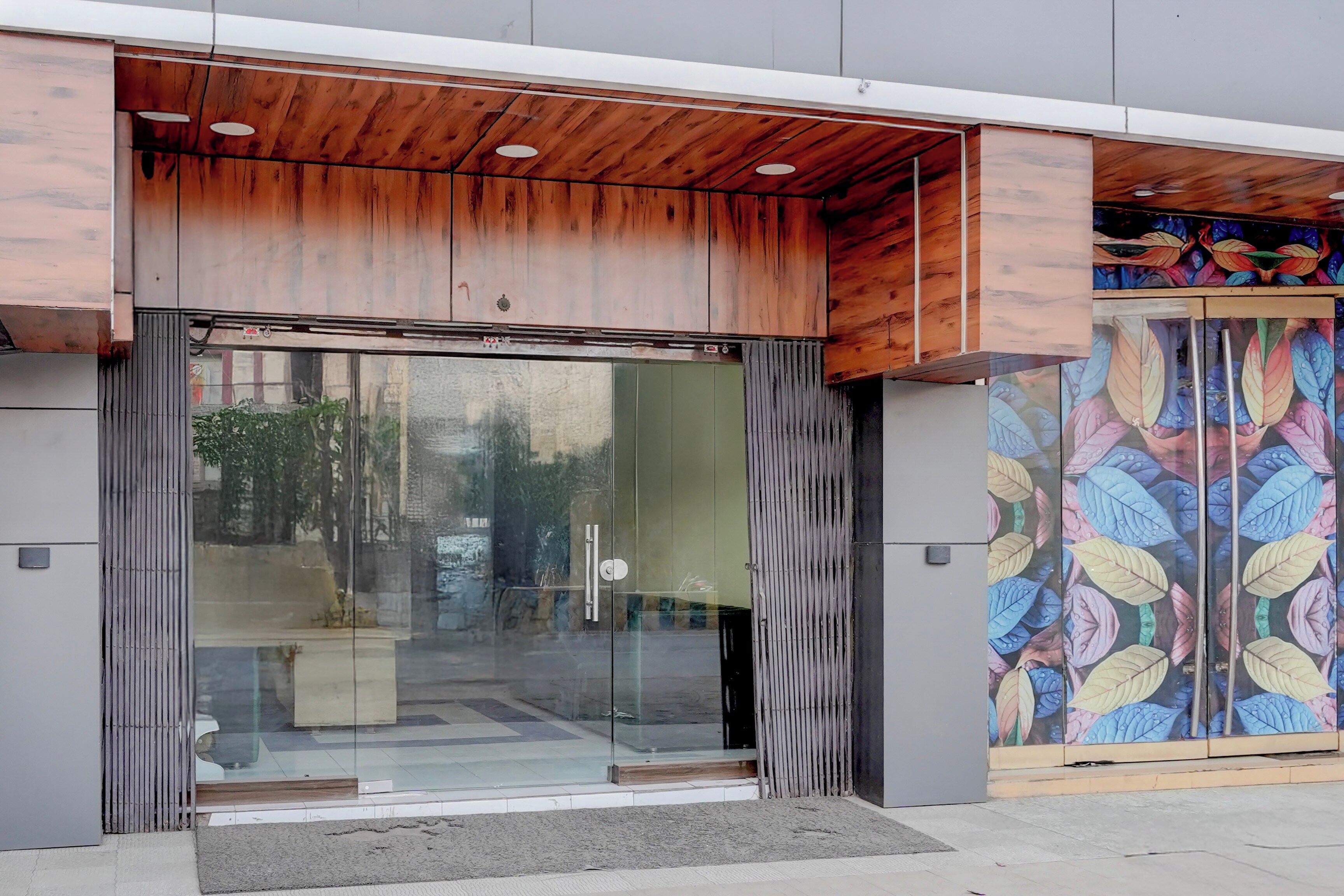 Una entrada moderna a un edificio con puerta de vidrio, techo de madera y pared con un estampado de hojas coloridas.