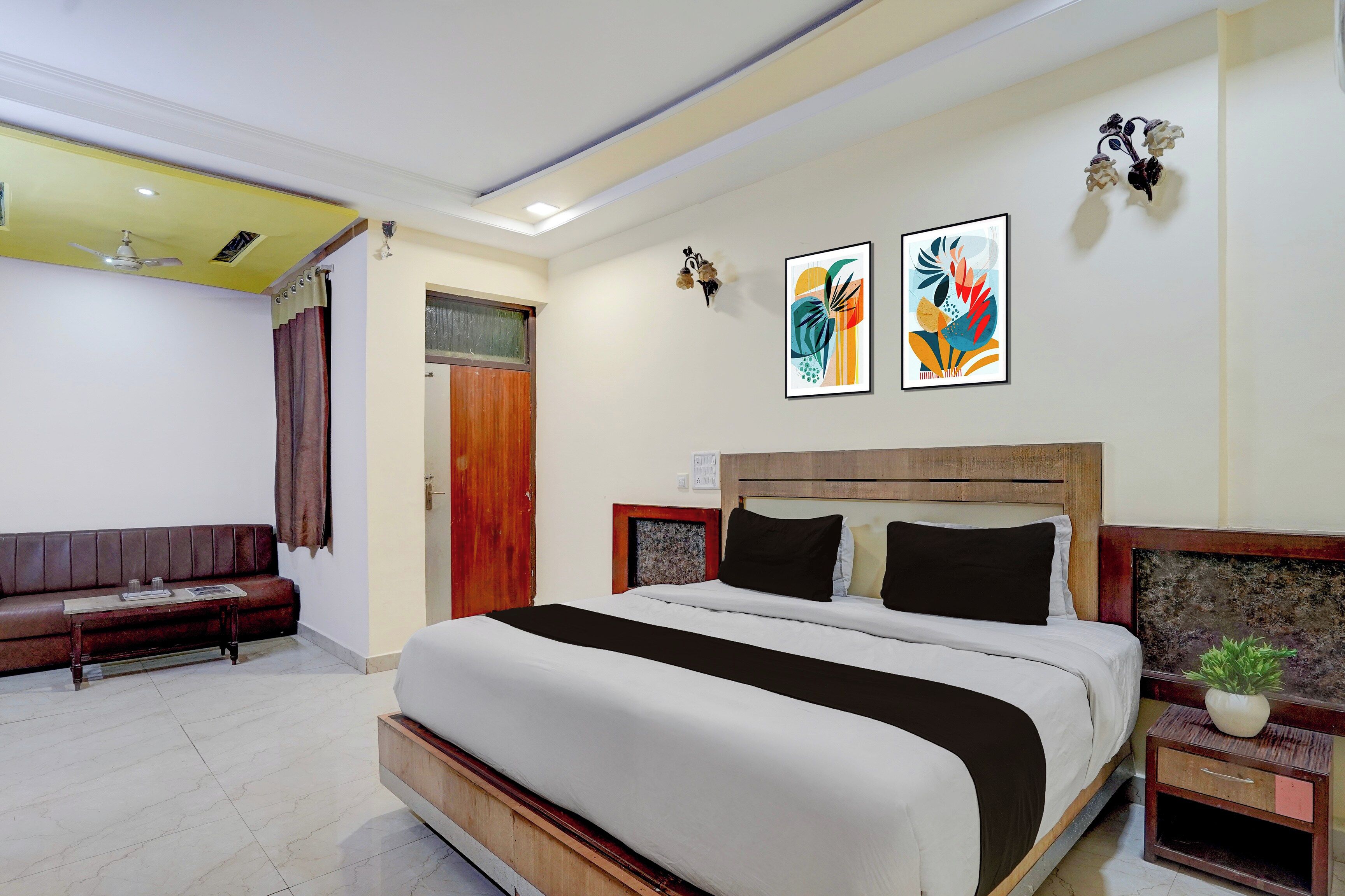 A hotel room with a bed, a sofa, a ceiling fan, and two wall-mounted artworks.